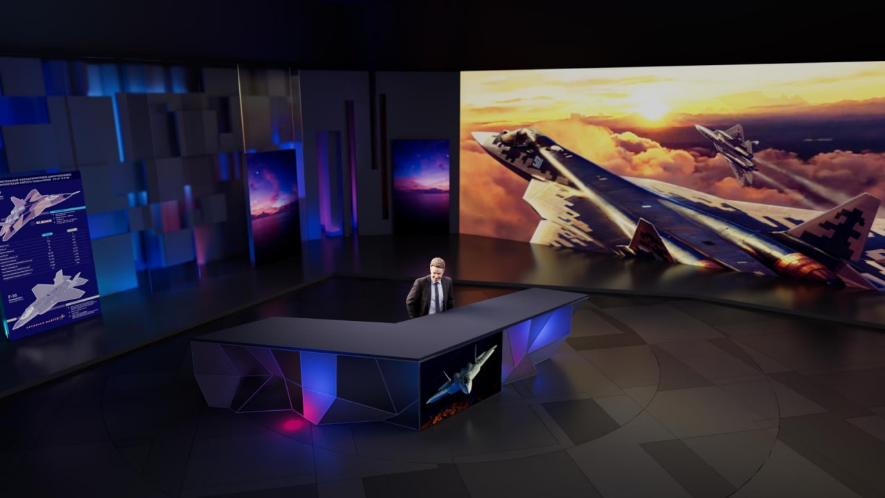 Angular desk studio with a large wall-scale display image and dark blue scenic contrast.